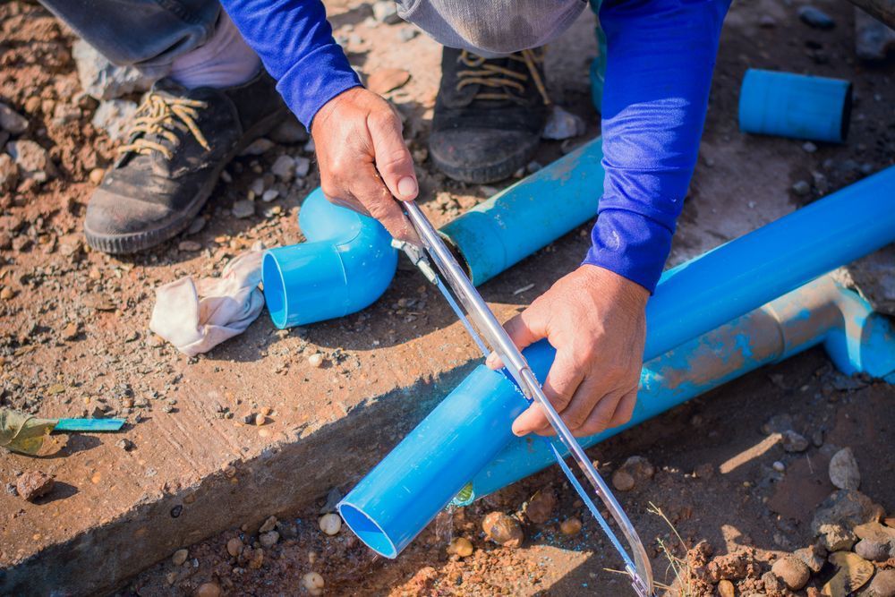 A Man is Cutting a Blue Pvc Pipe With a Pair of Scissors — Gold Coast Leak Detection in Mudgeeraba, QLD
