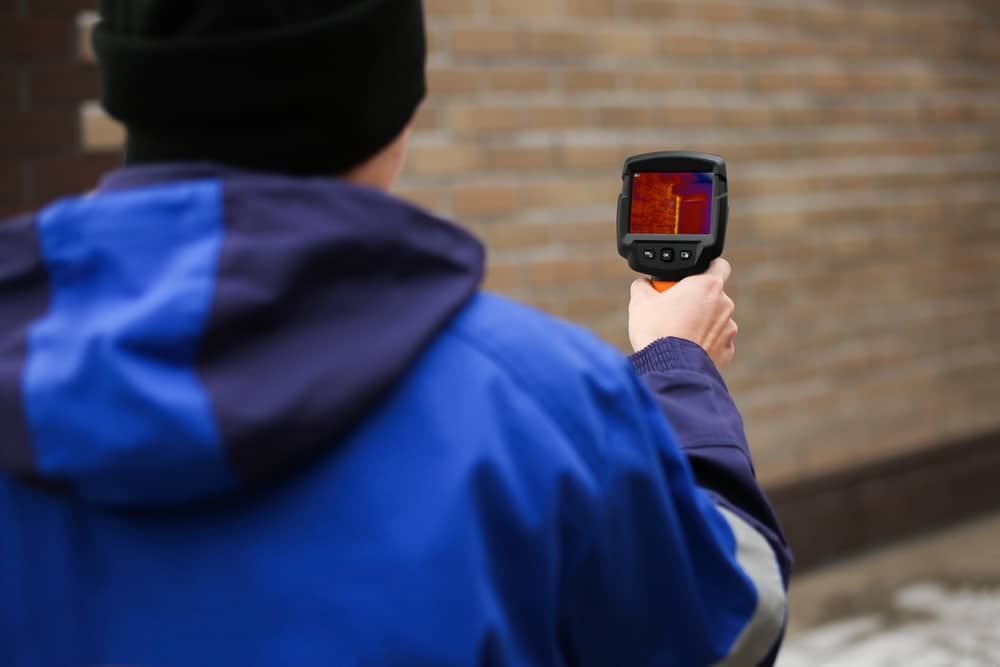 A Man is Holding a Thermal Camera in Front of a Brick Wall — Gold Coast Leak Detection in Mudgeeraba, QLD