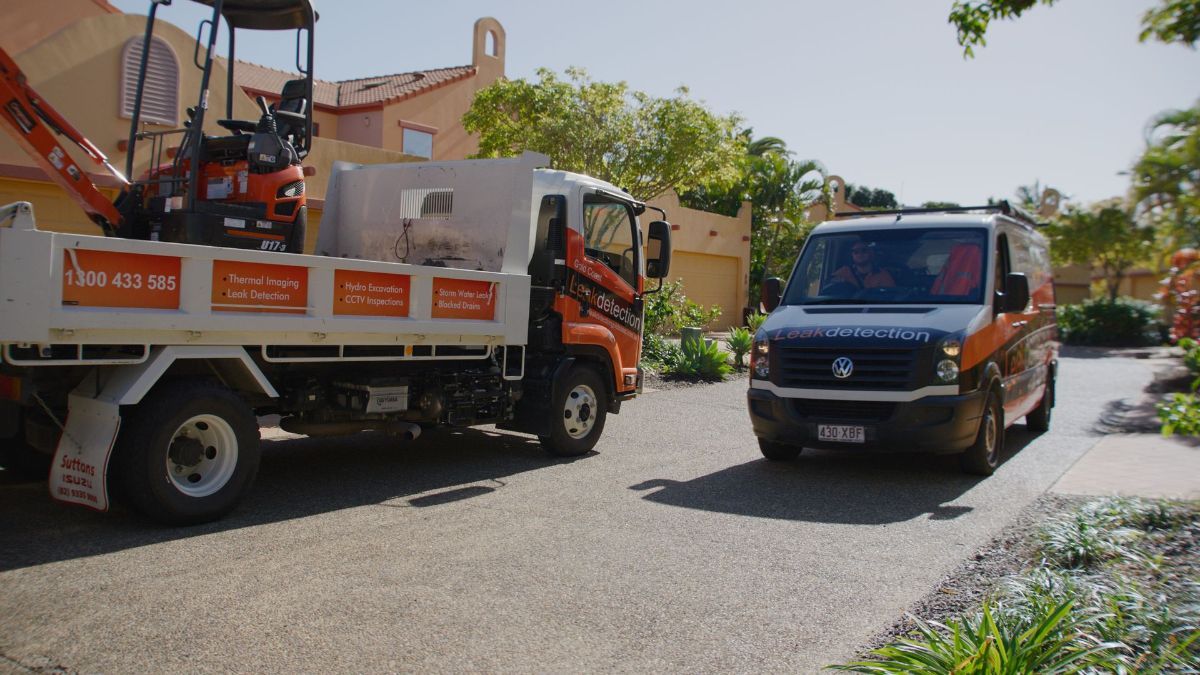 Leak detection service vehicles, including a truck with equipment and a van, parked in a driveway.