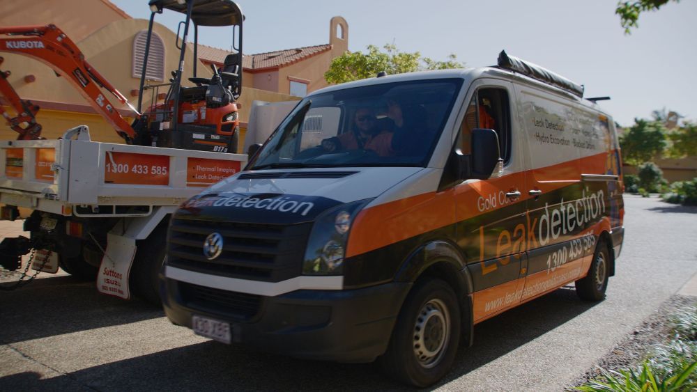A Man in Orange Overalls is Standing Next to a Manhole — Gold Coast Leak Detection in Mudgeeraba, QLD