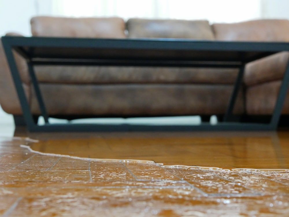 Low Angle Of Wet Wood Floor With A Metal-framed Coffee Table And Leather Sofa In The Background