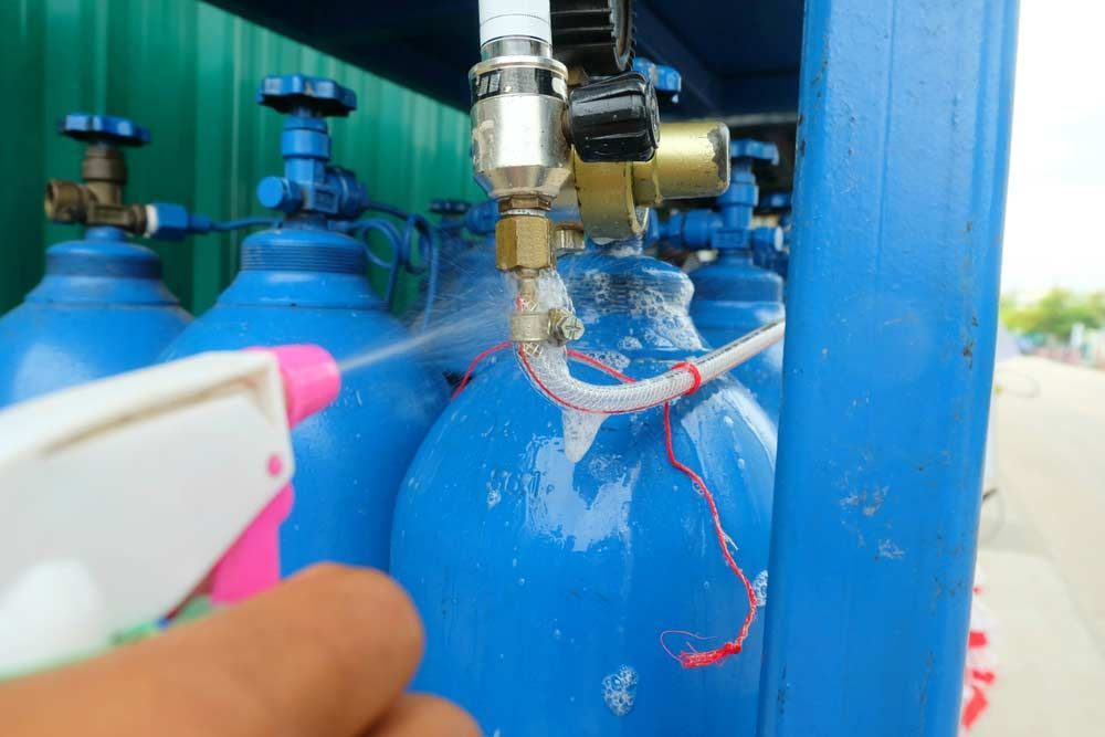 A Person Is Spraying A Blue Cylinder With A Pink Spray Bottle — Gold Coast Leak Detection In Mudgeeraba, QLD
