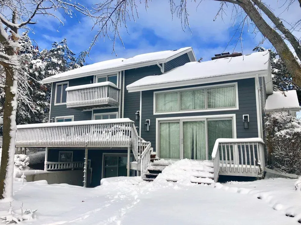 A large house is covered in snow on a sunny day.