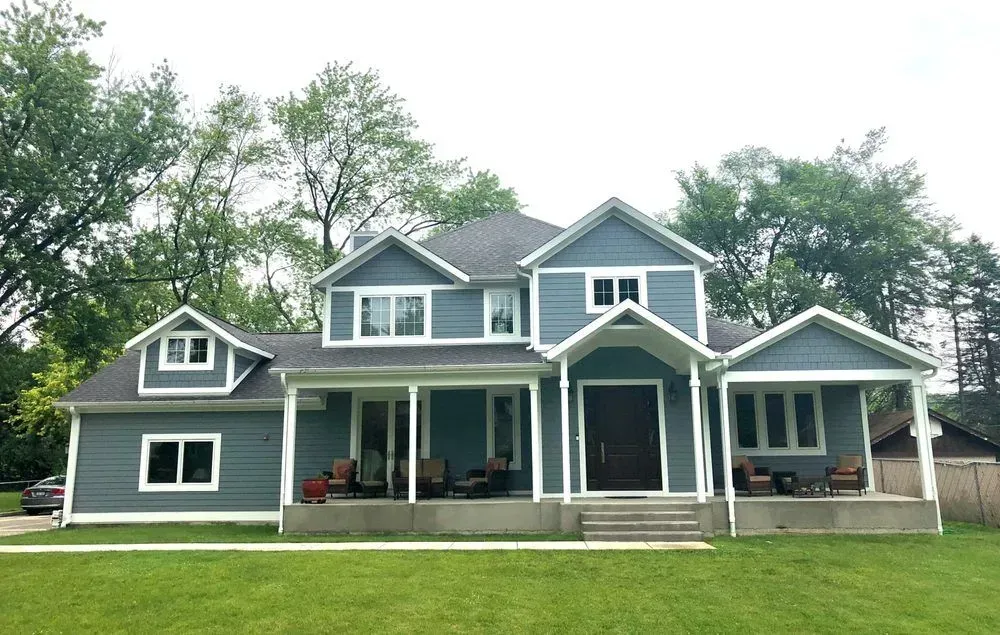 A large blue house with a porch and trees in the background