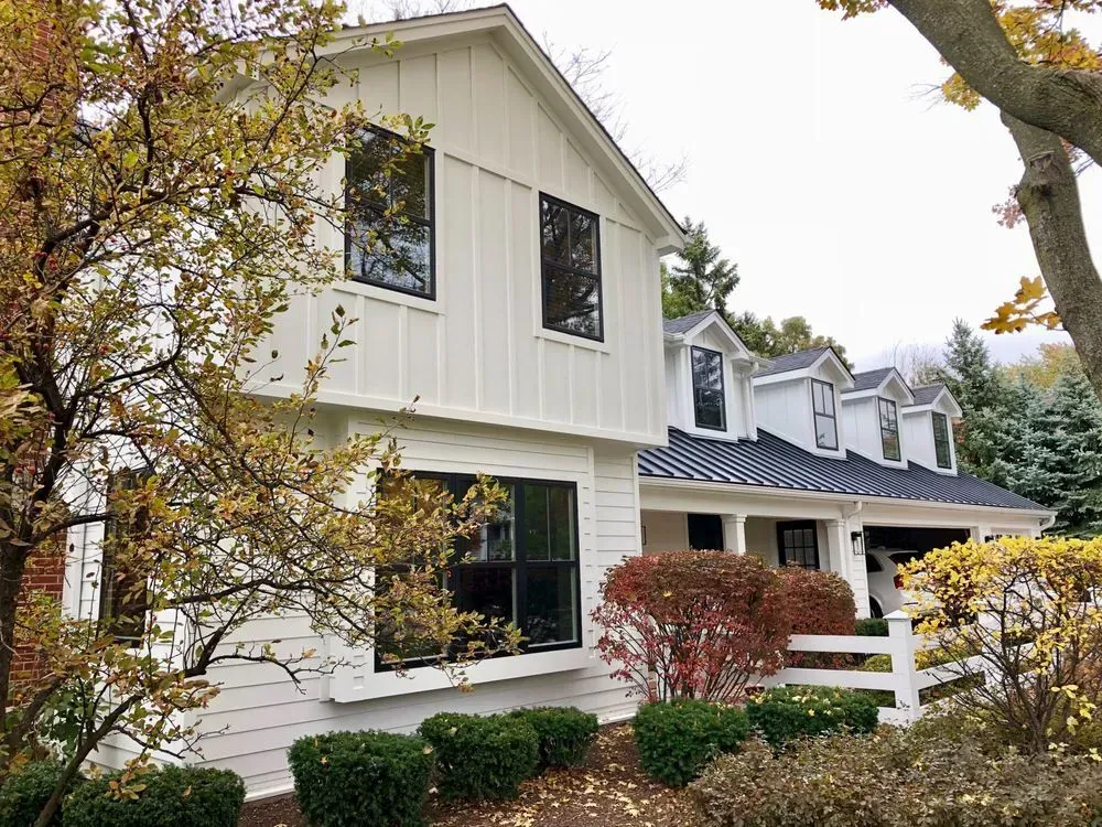 A white house with a black roof is surrounded by trees and bushes.