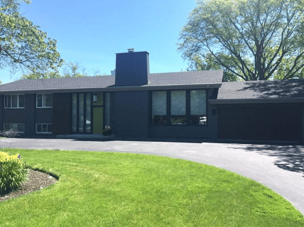 A black house with a gray roof is sitting on top of a lush green lawn.