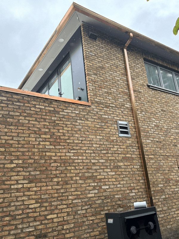 A brick building with a copper gutter on the side of it.