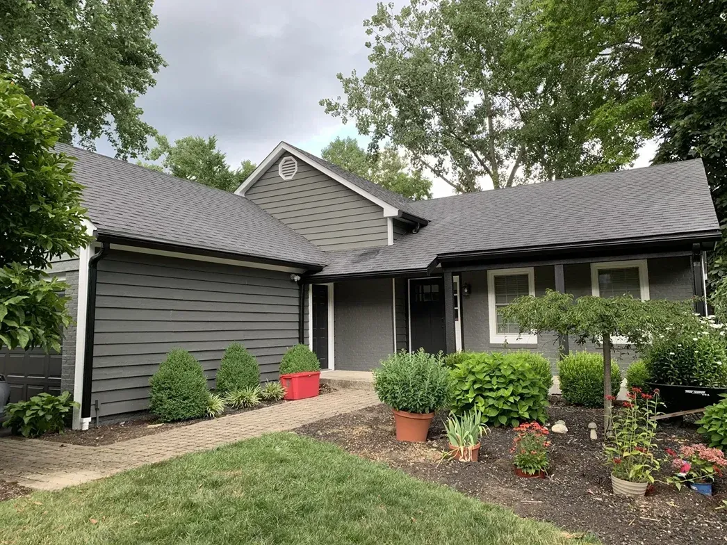 A gray house with a gray roof is surrounded by trees and bushes.