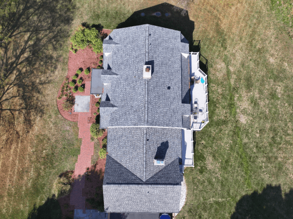 An aerial view of a house with a gray roof and a red brick driveway.