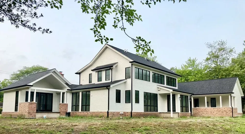 A large white house with a black roof is sitting on top of a lush green field.