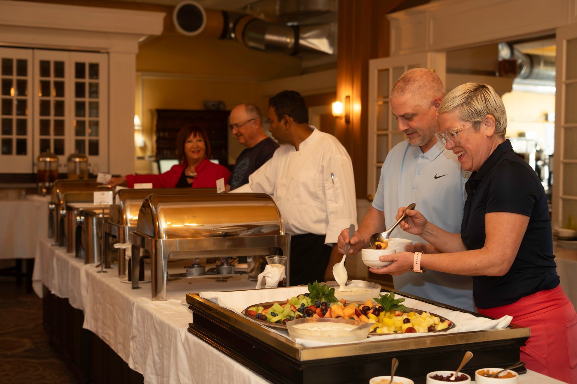 A group of people are standing around a buffet table eating food.