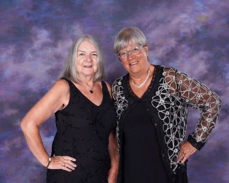 Two women are posing for a picture in front of a purple background.