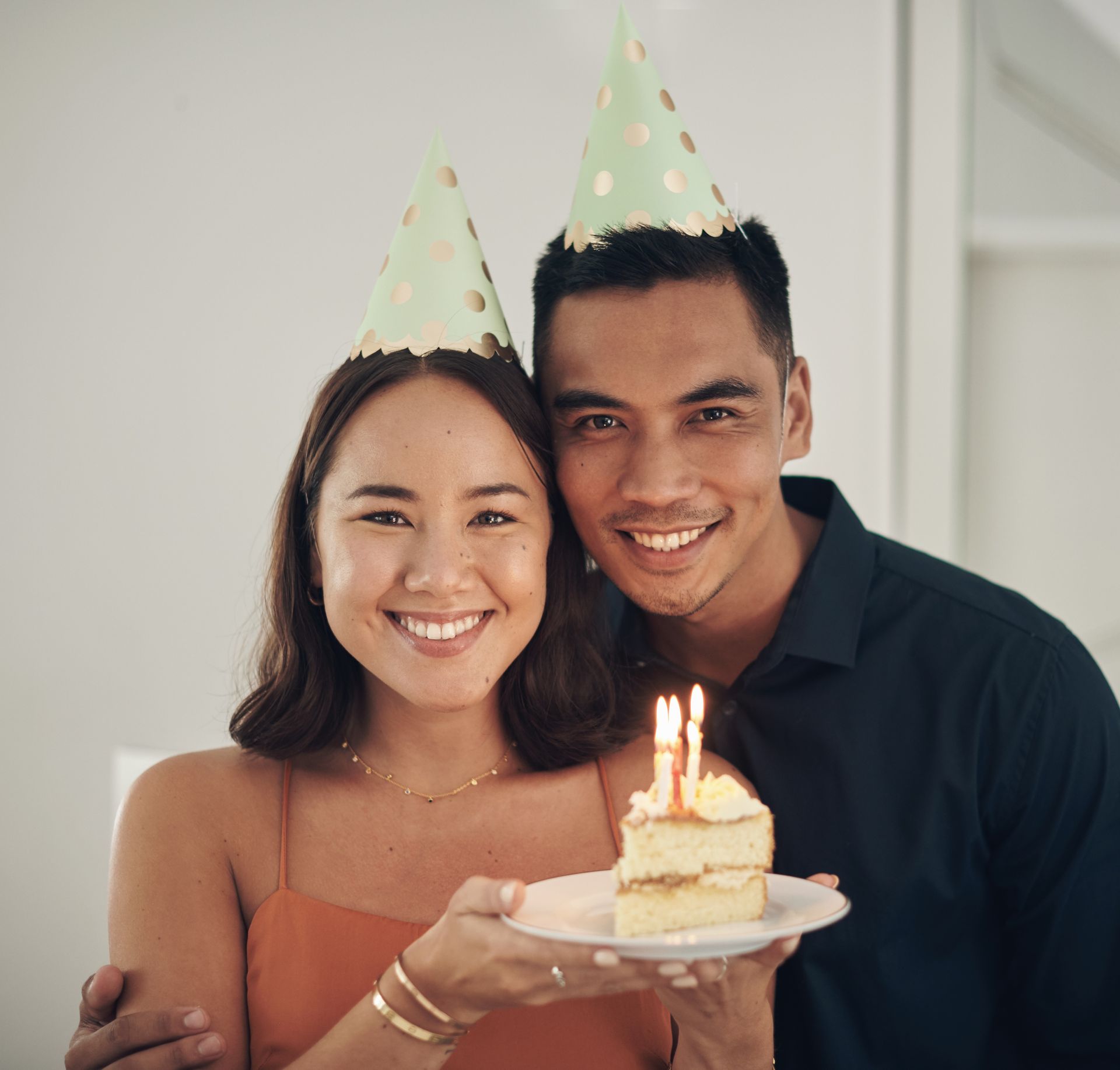 A man and a woman wearing party hats are holding a birthday cake