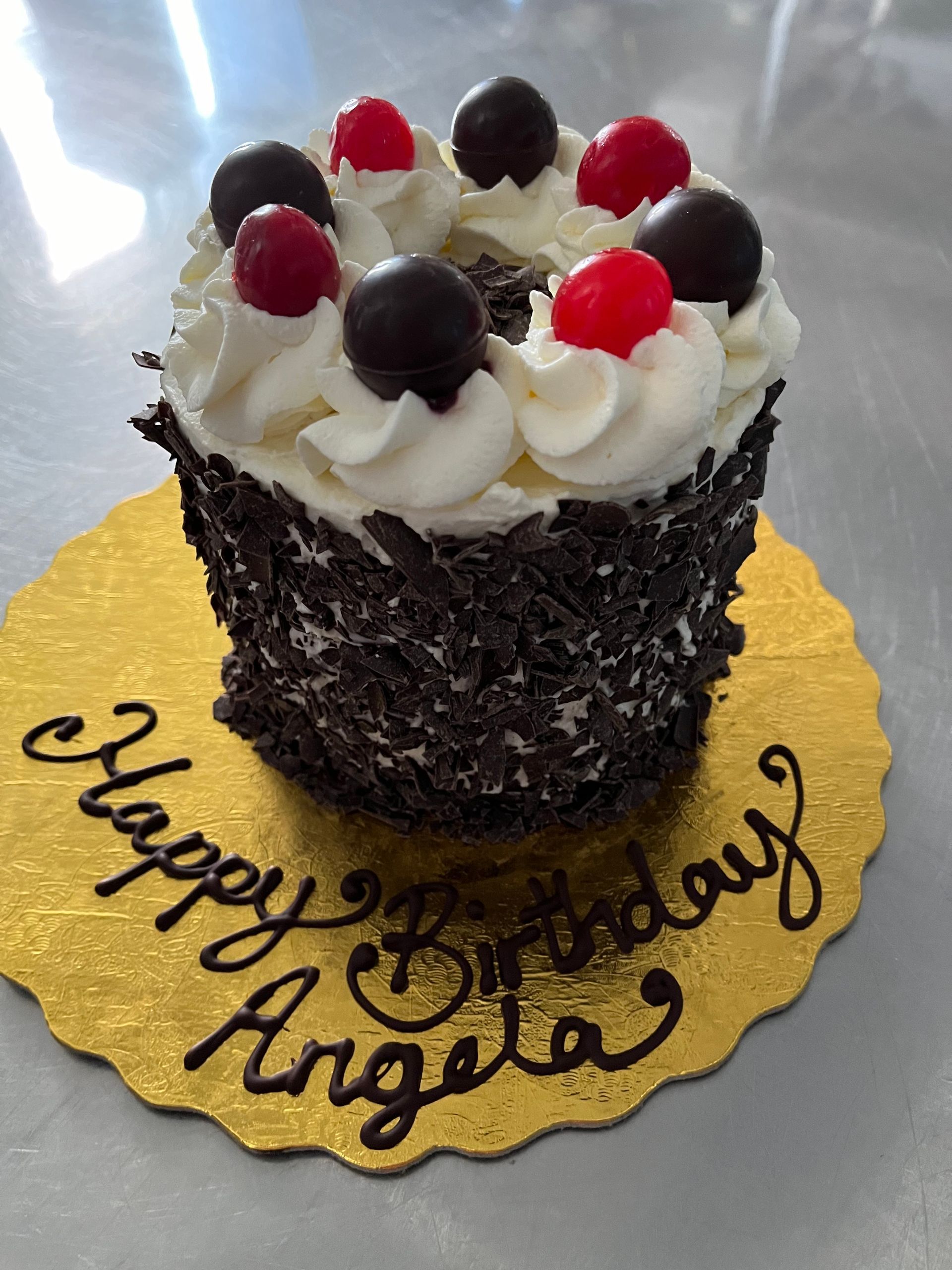 A birthday cake with cherries and whipped cream says happy birthday angela
