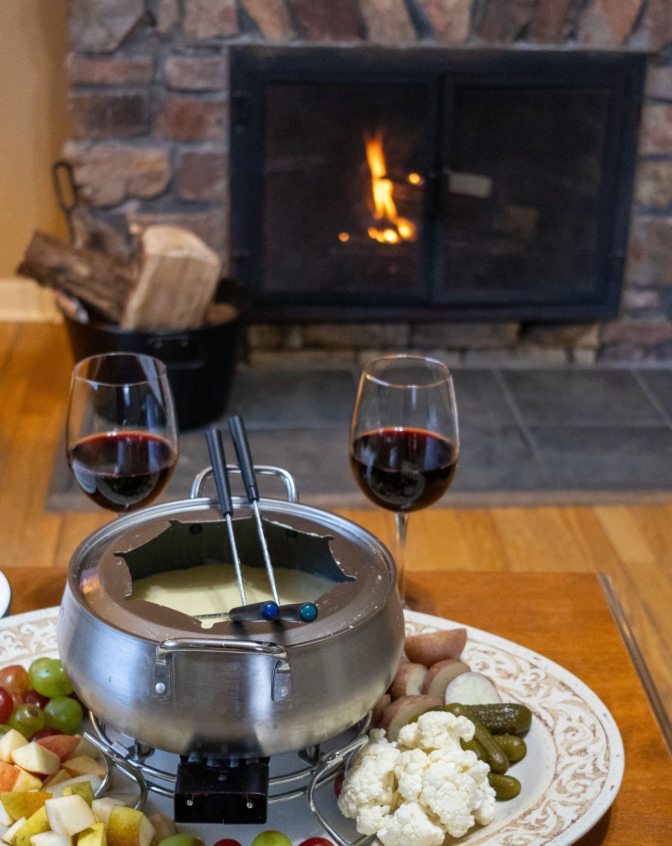 A fondue is being cooked in front of a fireplace with two glasses of wine.