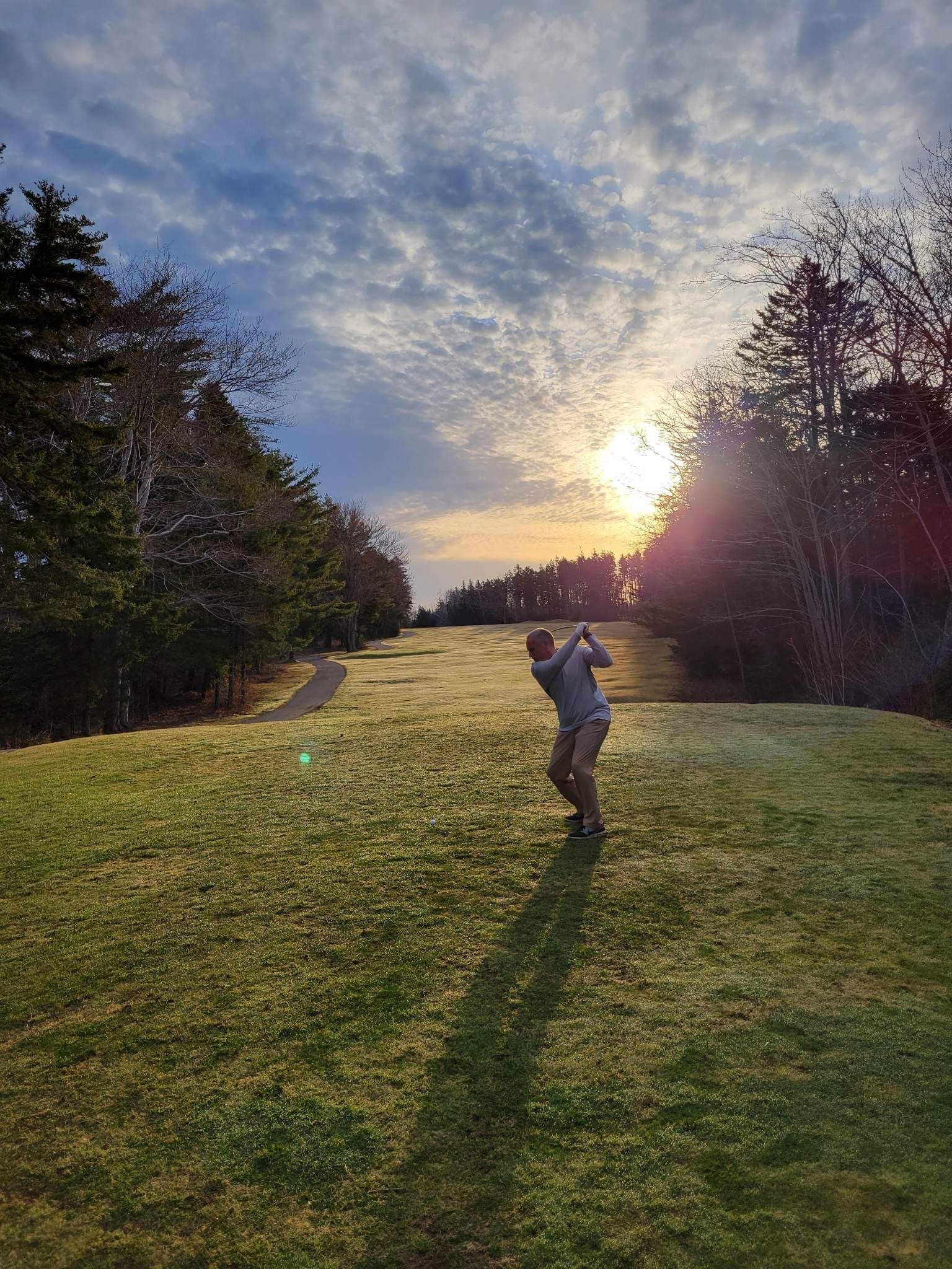 A man is swinging a golf club on a golf course at sunset.