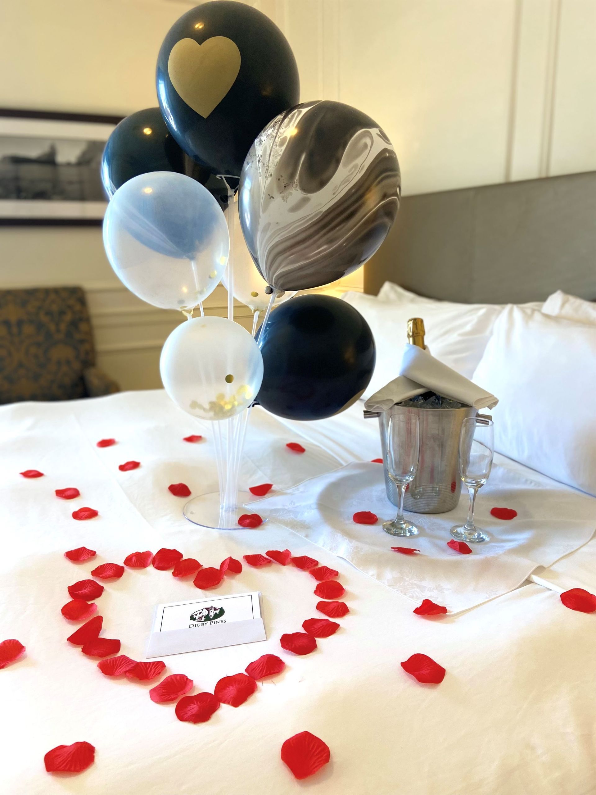 A bed with balloons and rose petals on it