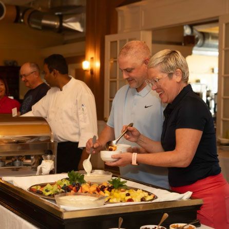 A group of people are standing around a buffet table eating food.