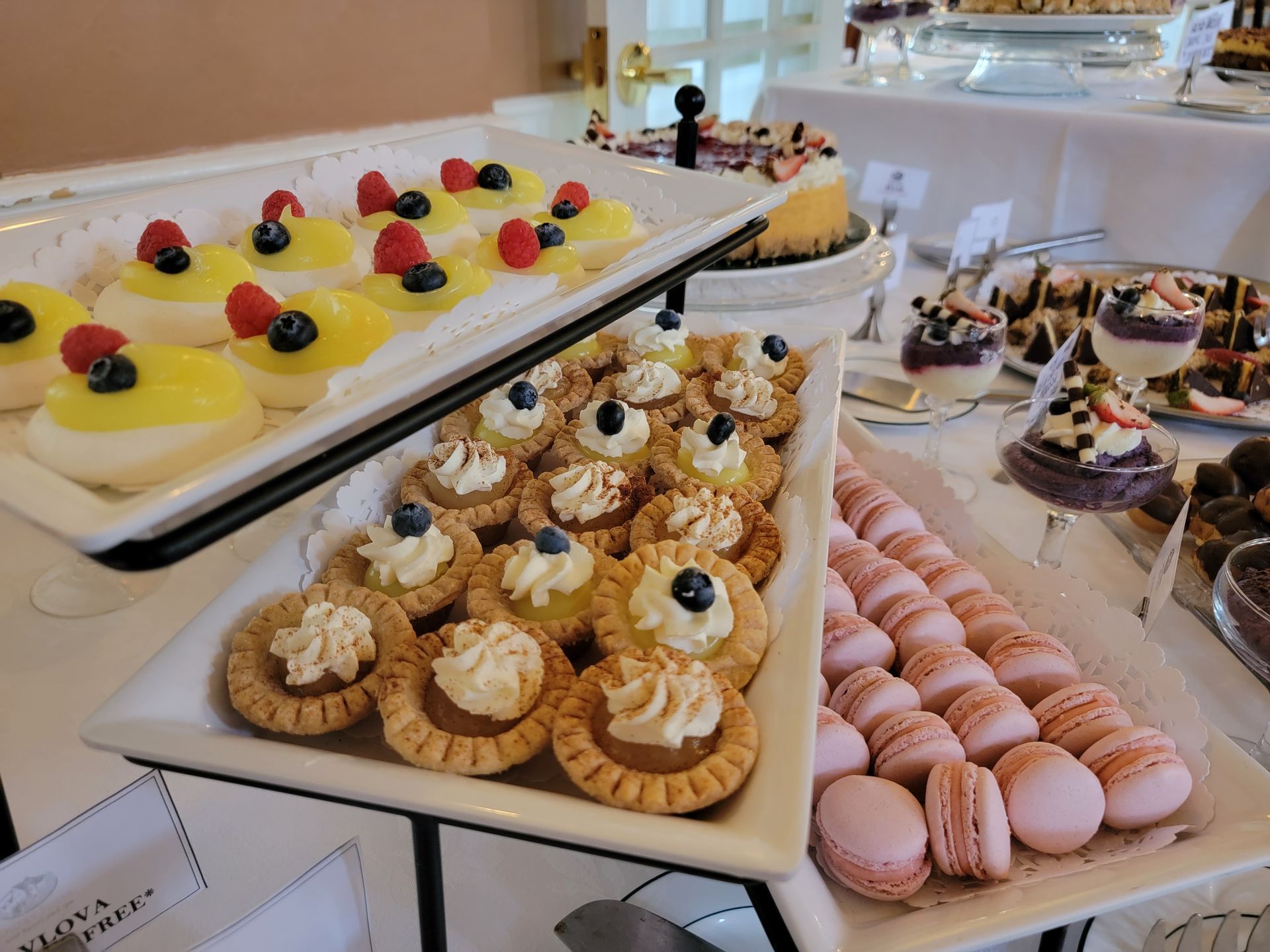 A tiered dessert display featuring small tarts with cream, berries, yellow-topped pastries, and pink macarons.