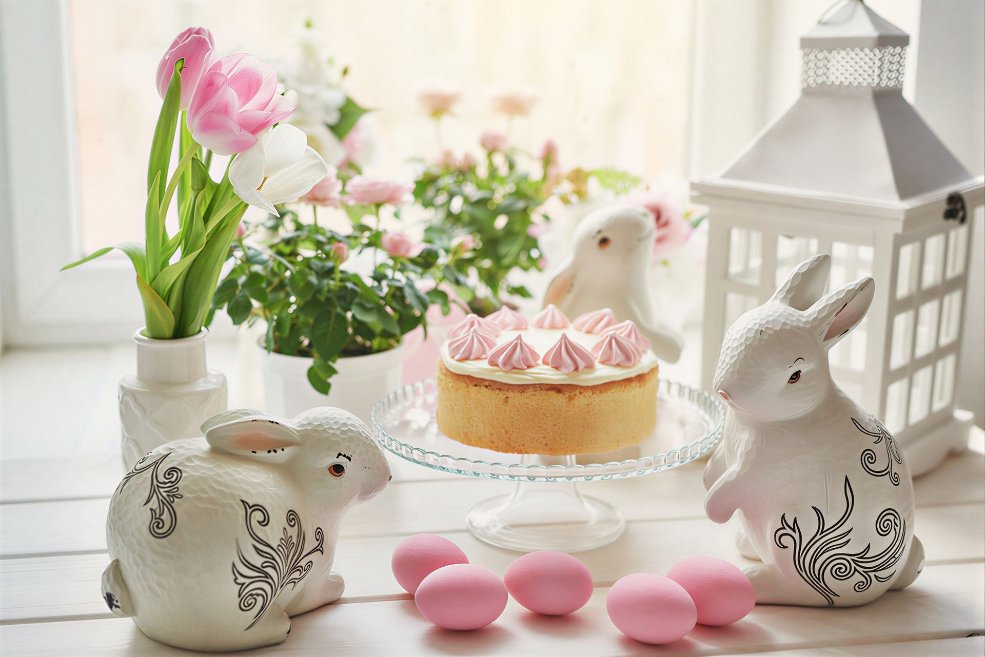 A white bunny with a large pink bow, sitting next to a basket of colorful Easter eggs on green faux grass.