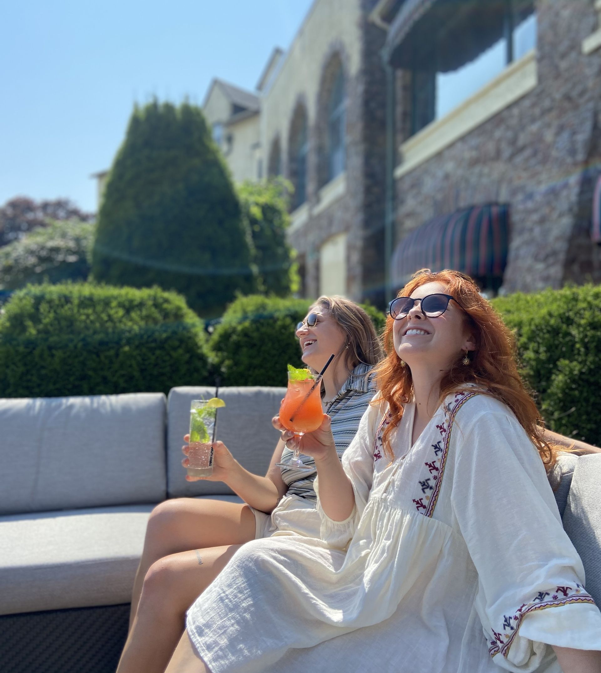 Two women are sitting on a couch holding drinks.