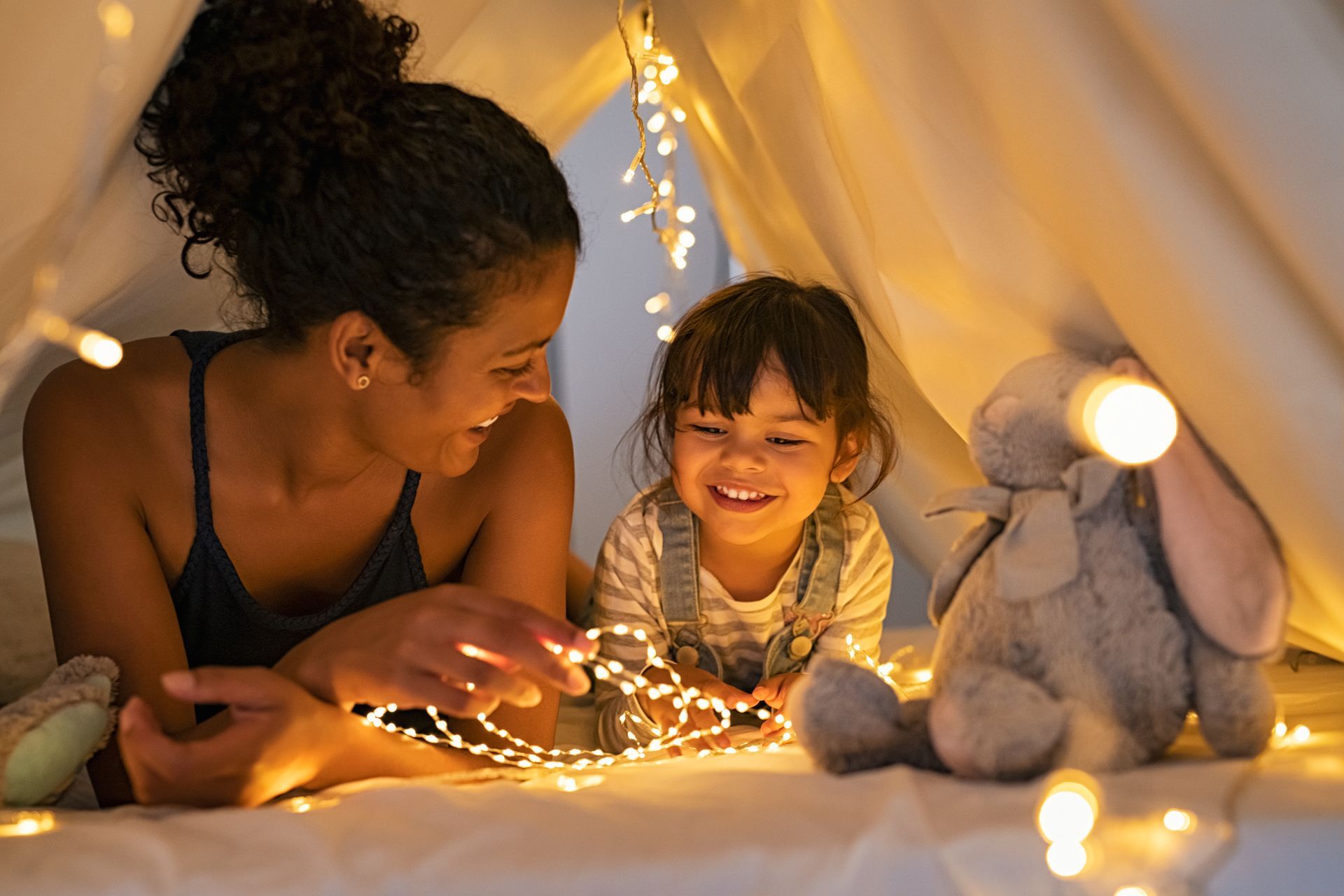 A woman and a little girl are laying in a tent with christmas lights.