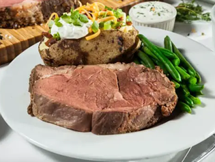 Plate of prime rib, green beans and a loaded baked potato.