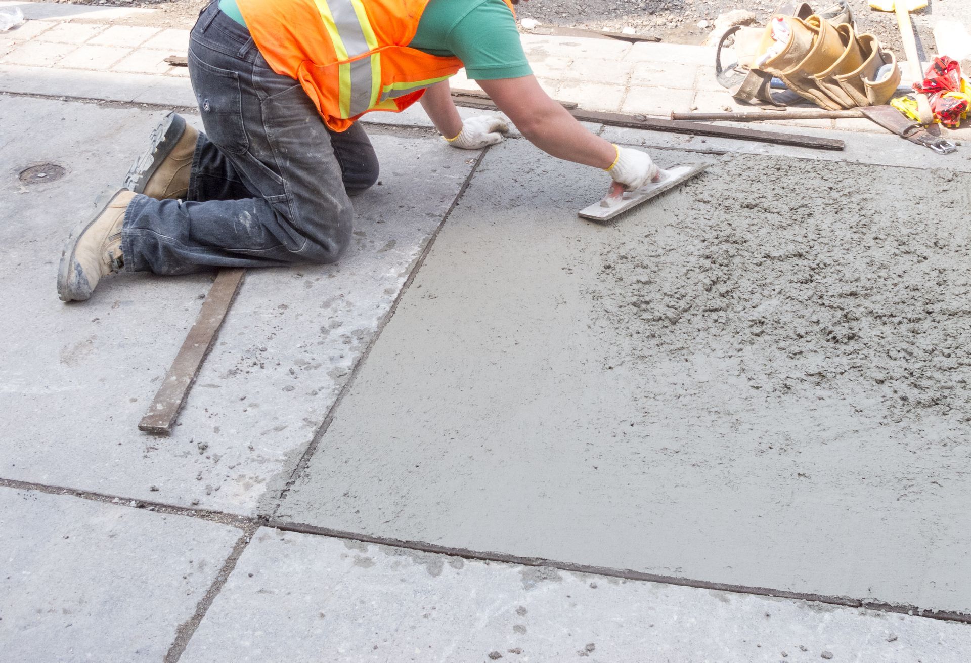 A construction worker is kneeling down and spreading concrete with a trowel