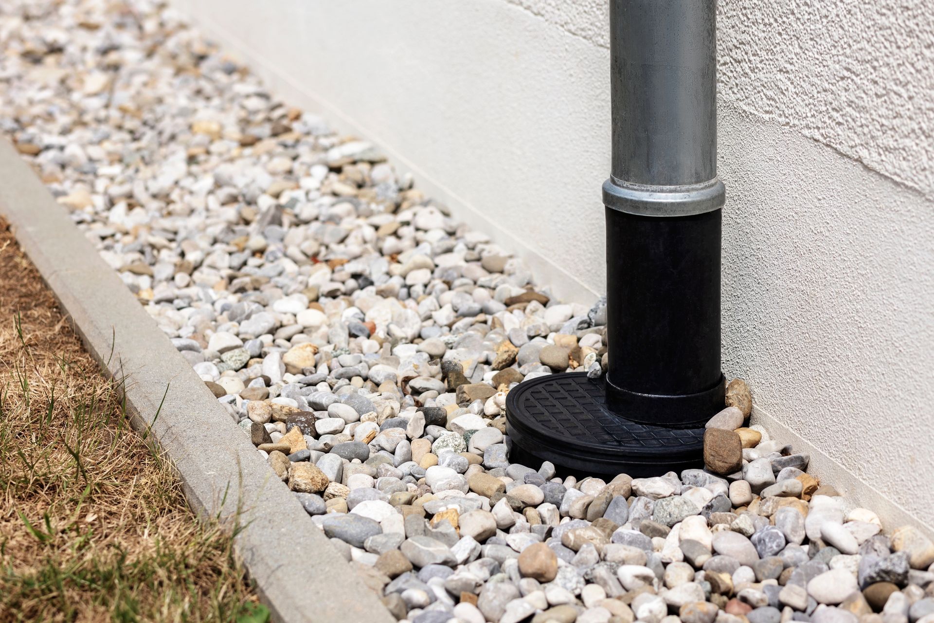 A black pipe is sitting on top of a pile of gravel next to a sidewalk.