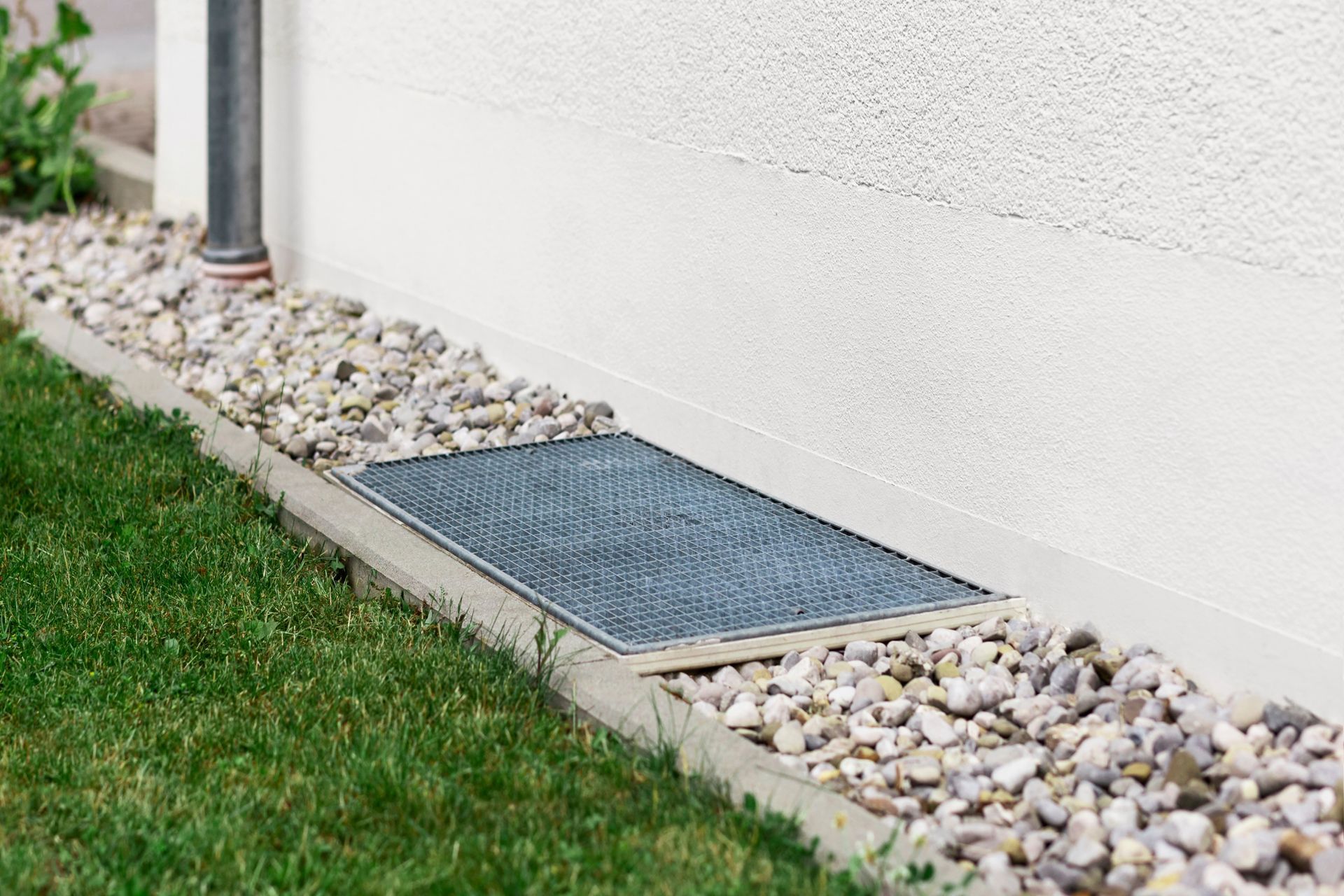 A sidewalk filled with gravel and a metal grate.