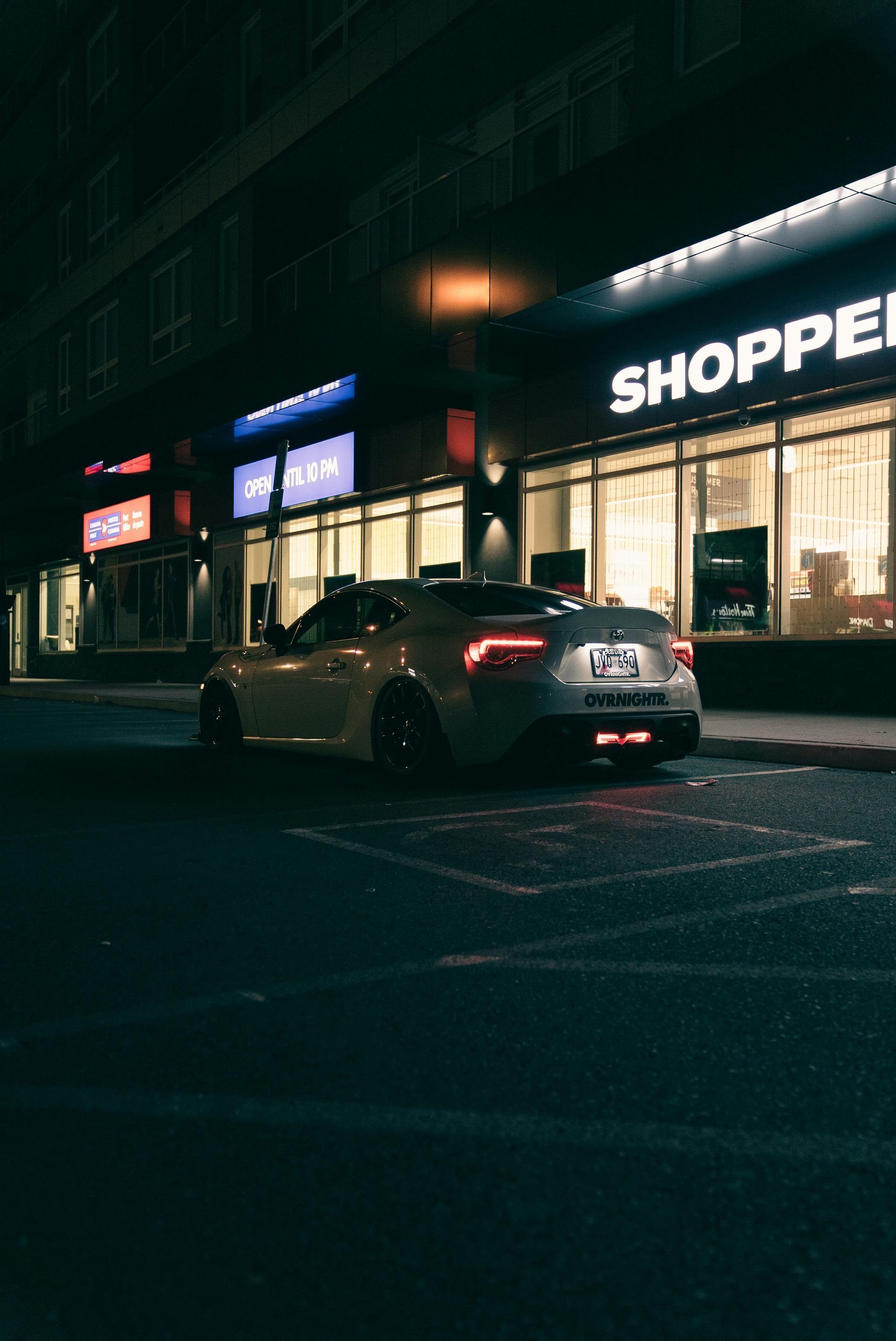 A car is parked in front of a shopping center at night.
