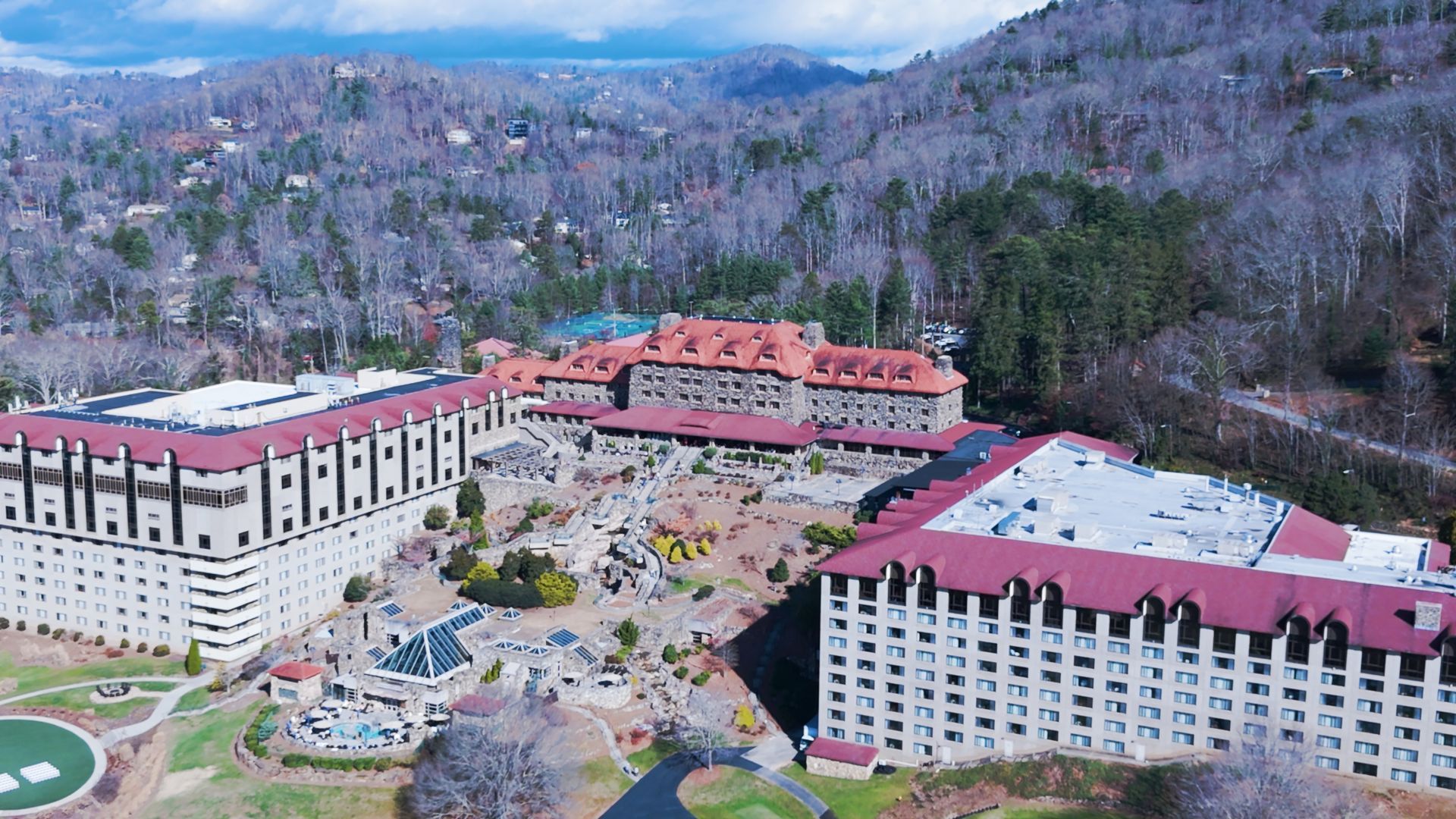 Aerial view of a large resort complex in the mountains, featuring multiple buildings with red roofs, surrounded by trees.