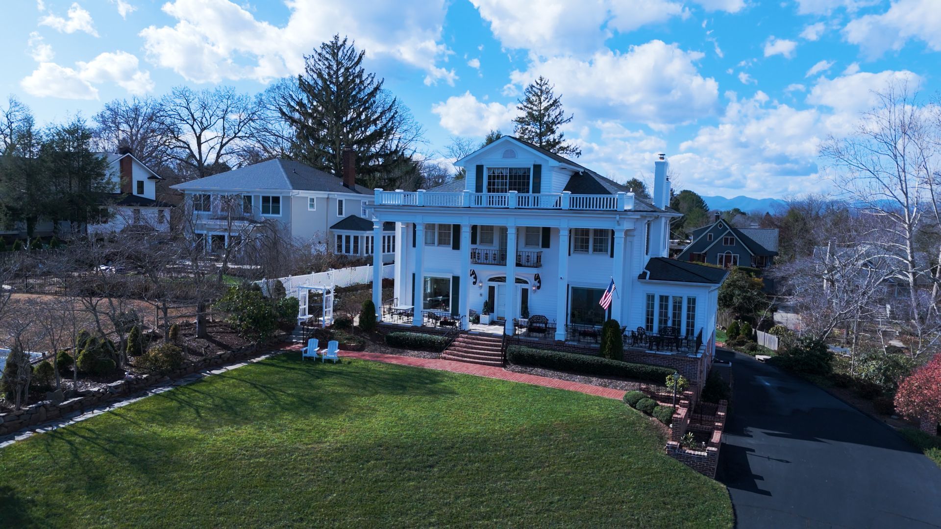 White two-story house with columns and a large lawn under a blue sky with clouds.