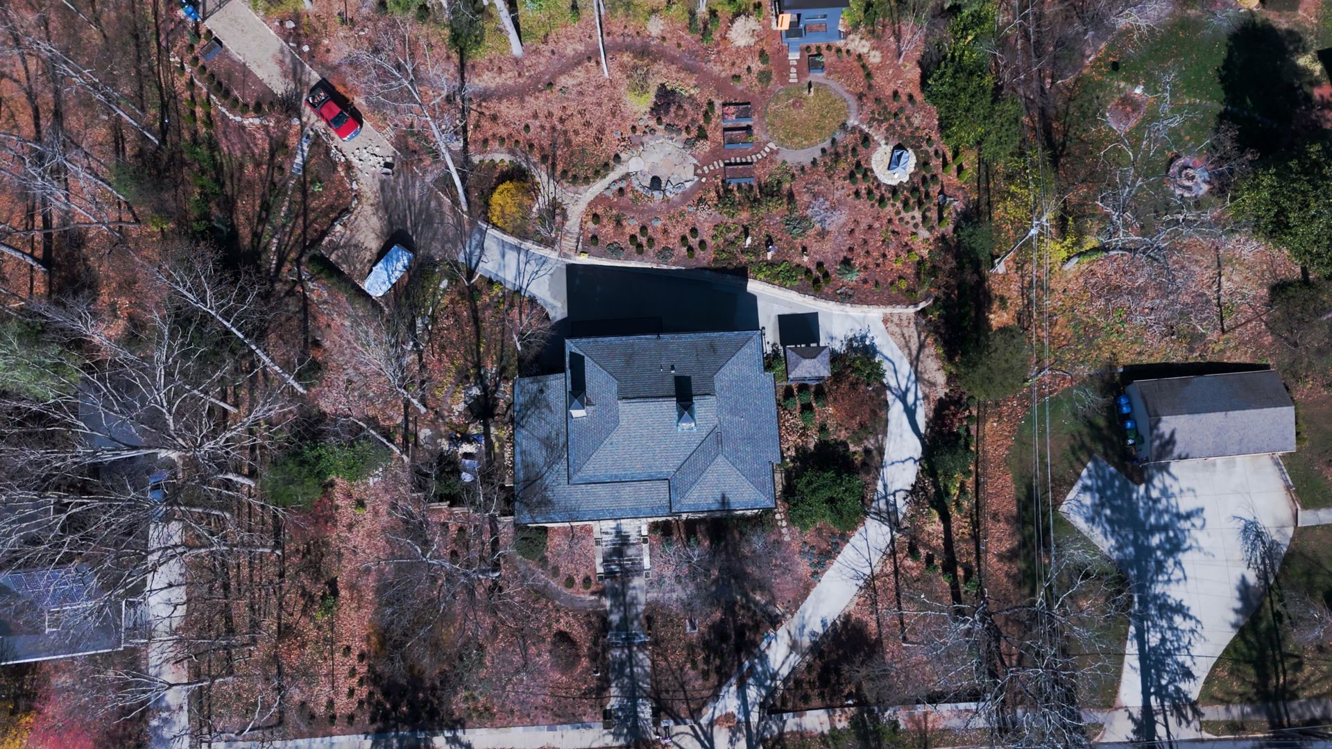 Overhead view of a house with a gray roof and winding walkways surrounded by brown foliage and a few cars.