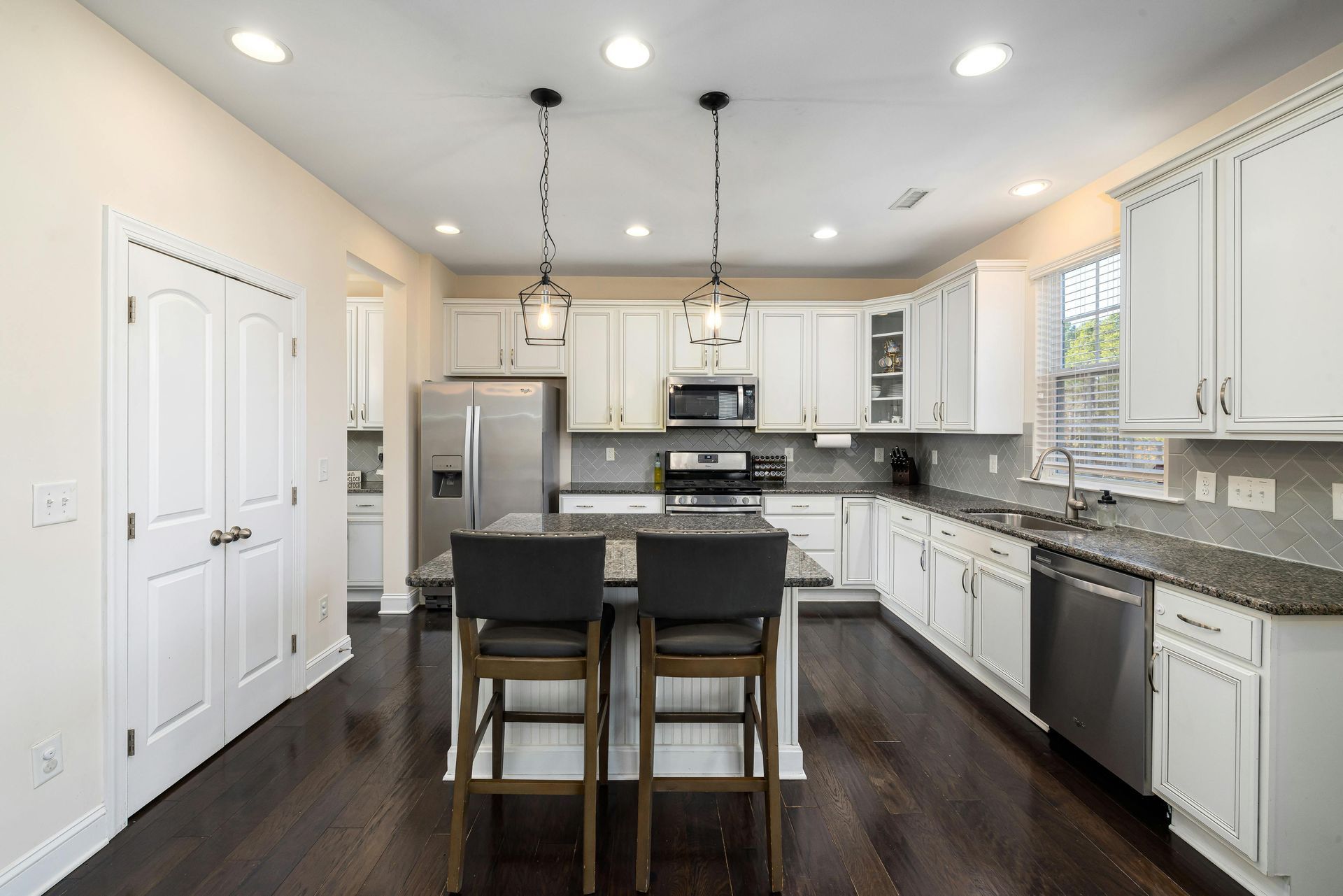 A bright white kitchen with a dark granite island, stainless steel appliances, and dark wood floors.