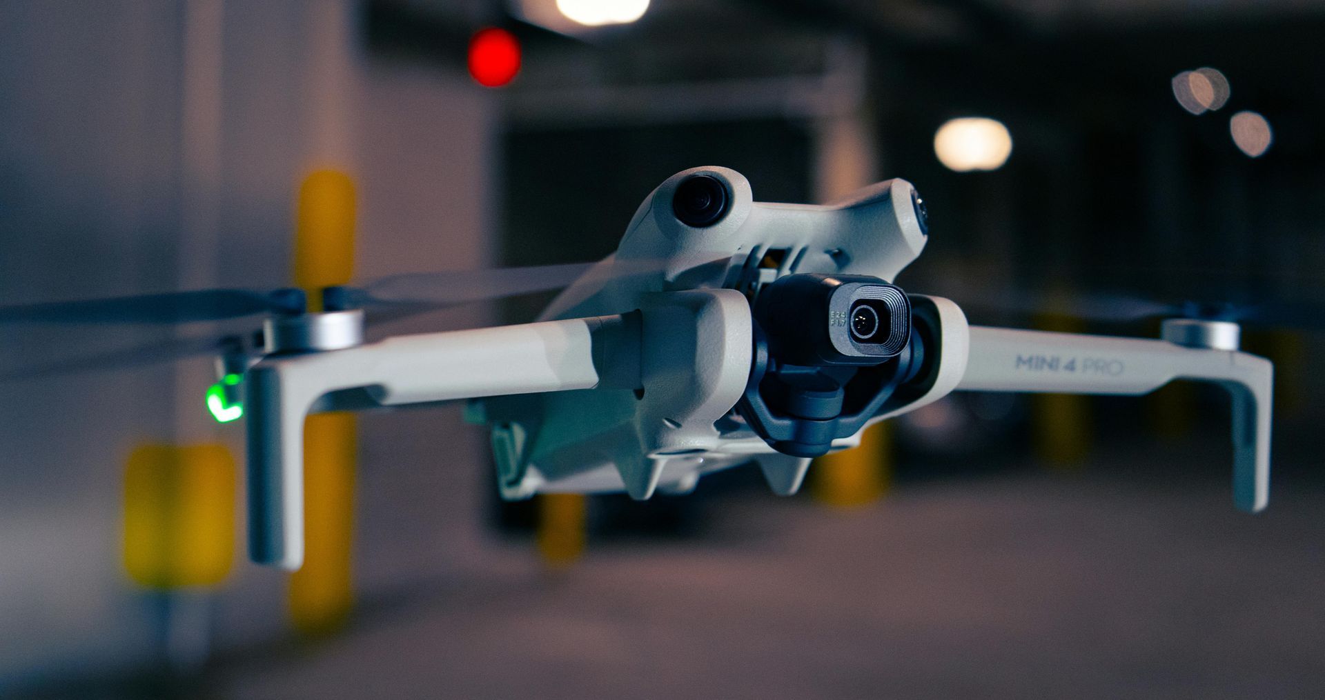 A white drone, DJI Mini 3 Pro, hovering in an indoor, dim setting. Its arms are extended, propellers spinning.
