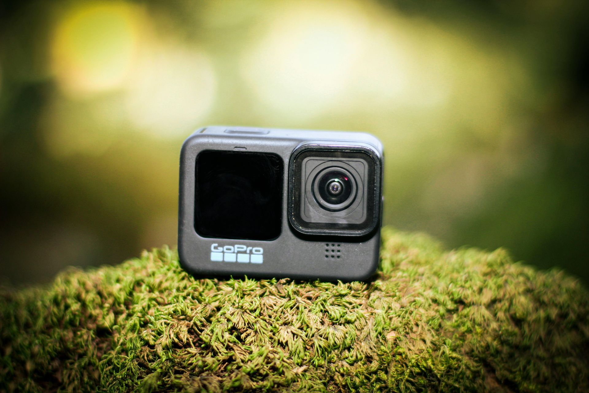 A black GoPro action camera rests on a patch of green moss in a soft-focus, outdoor environment.