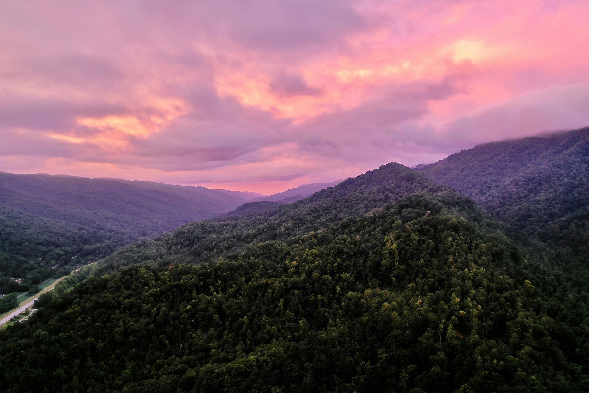 Mountains covered in dark green trees under a pink and purple sunset.