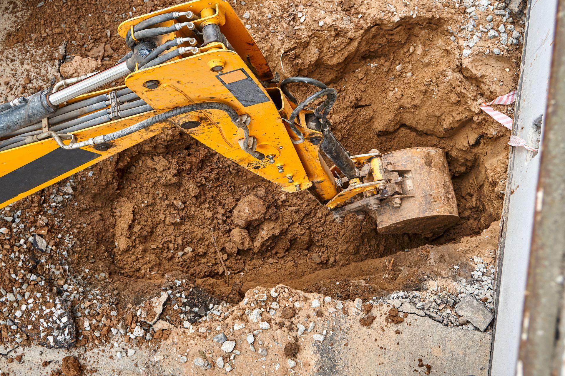 Yellow excavator digging a hole in the dirt, next to a concrete surface.