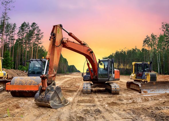 Construction site with heavy machinery like an excavator and bulldozer, against a colorful sunset.