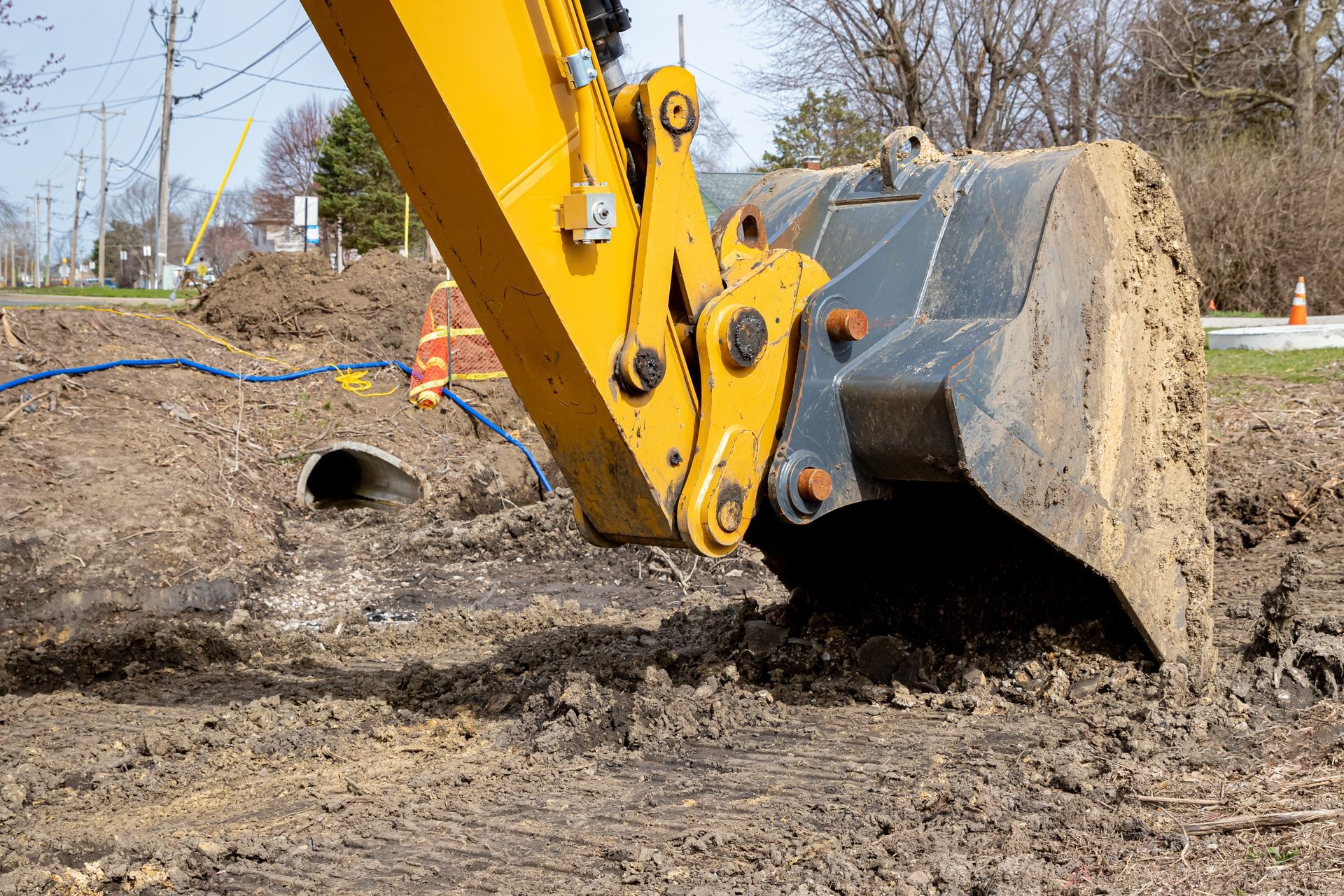 Yellow excavator bucket scooping dirt from a trench.