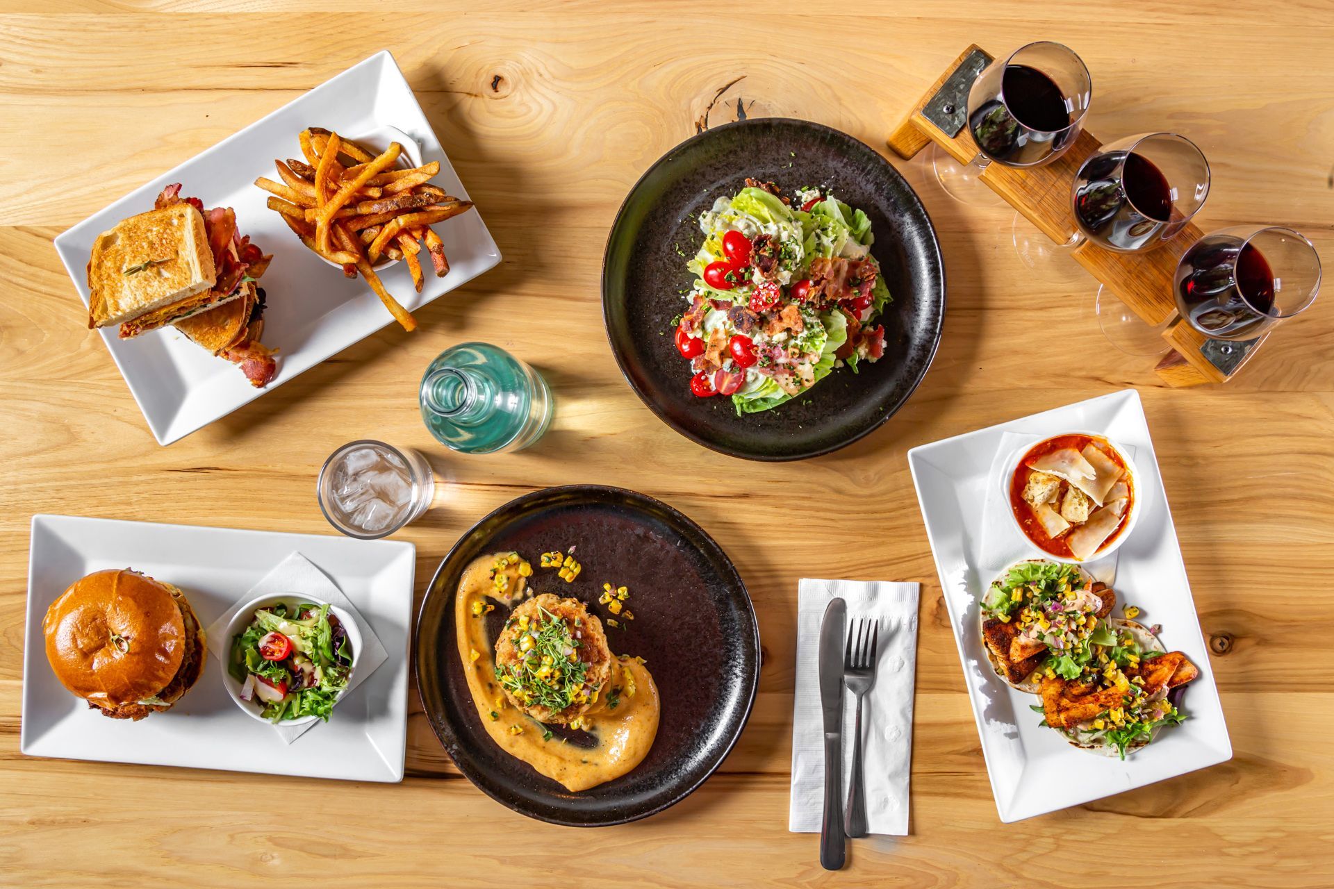 Overhead view of a restaurant table with various dishes like sandwiches, salad, and a wine flight.