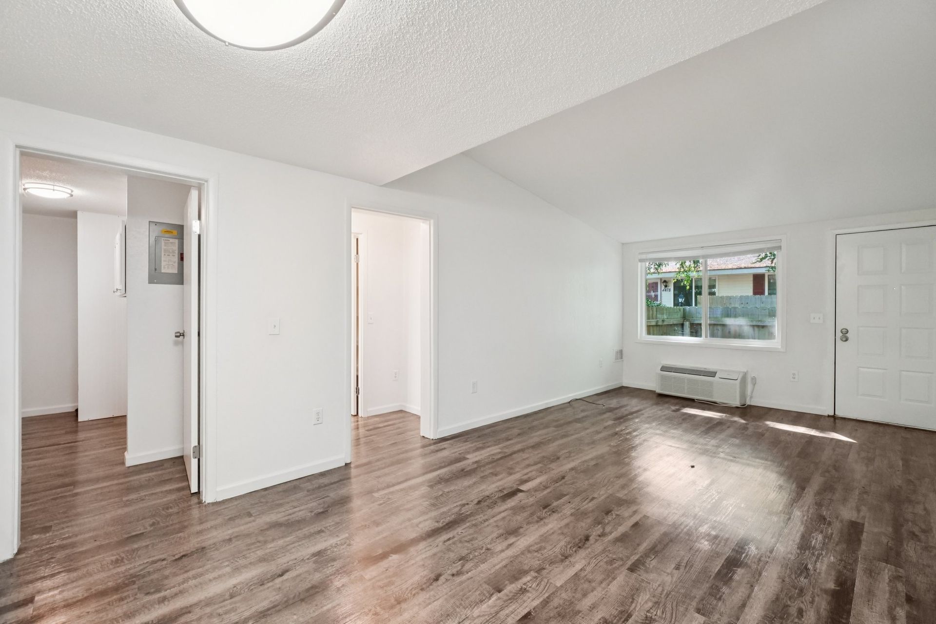 Empty apartment interior with wood flooring, white walls, and bright lighting.