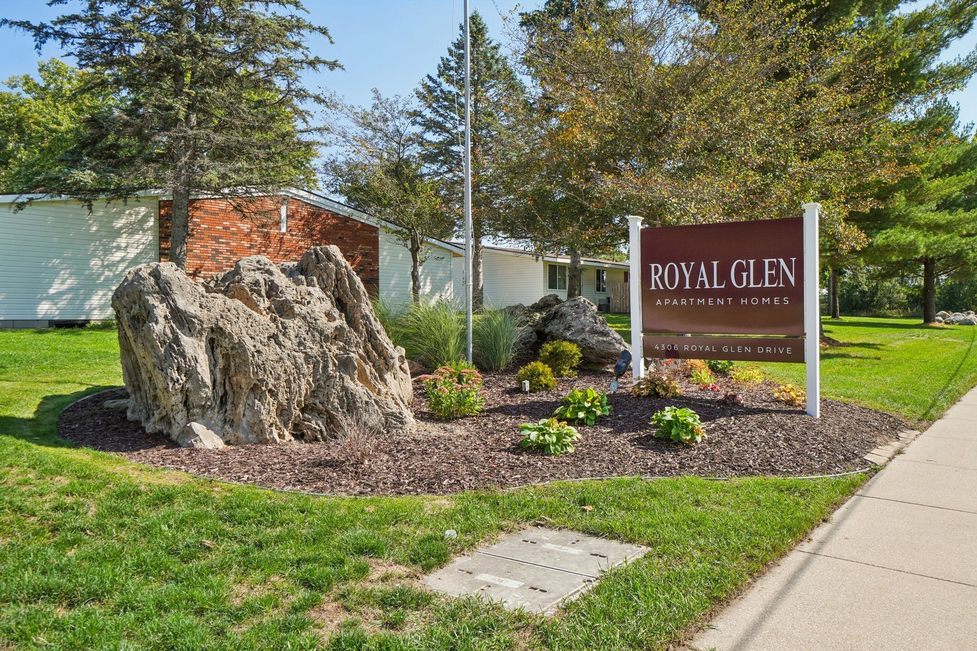 Sign for Royal Glen apartments with a large rock and landscaping.