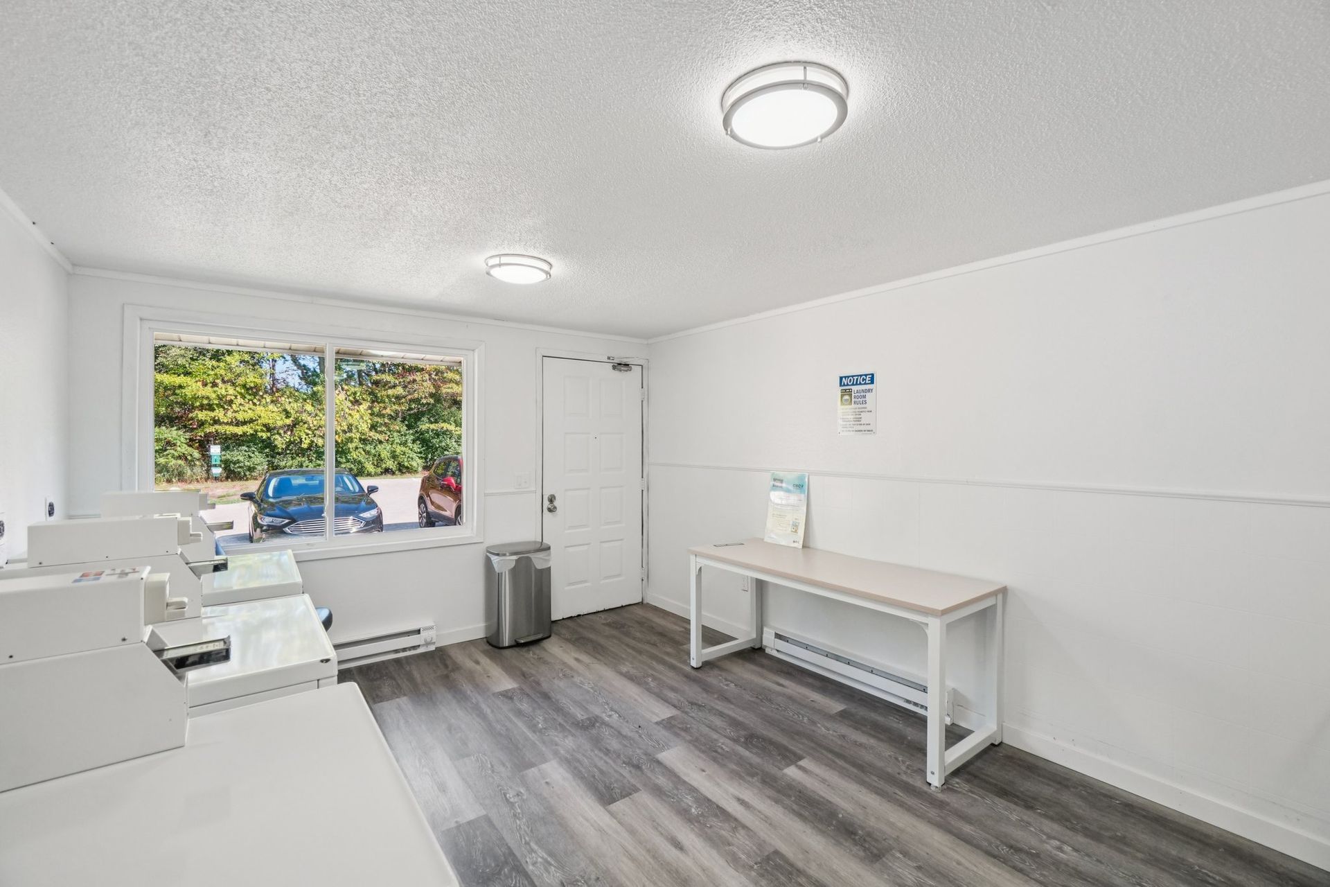 Laundry room with washers, a table, window, and gray flooring.