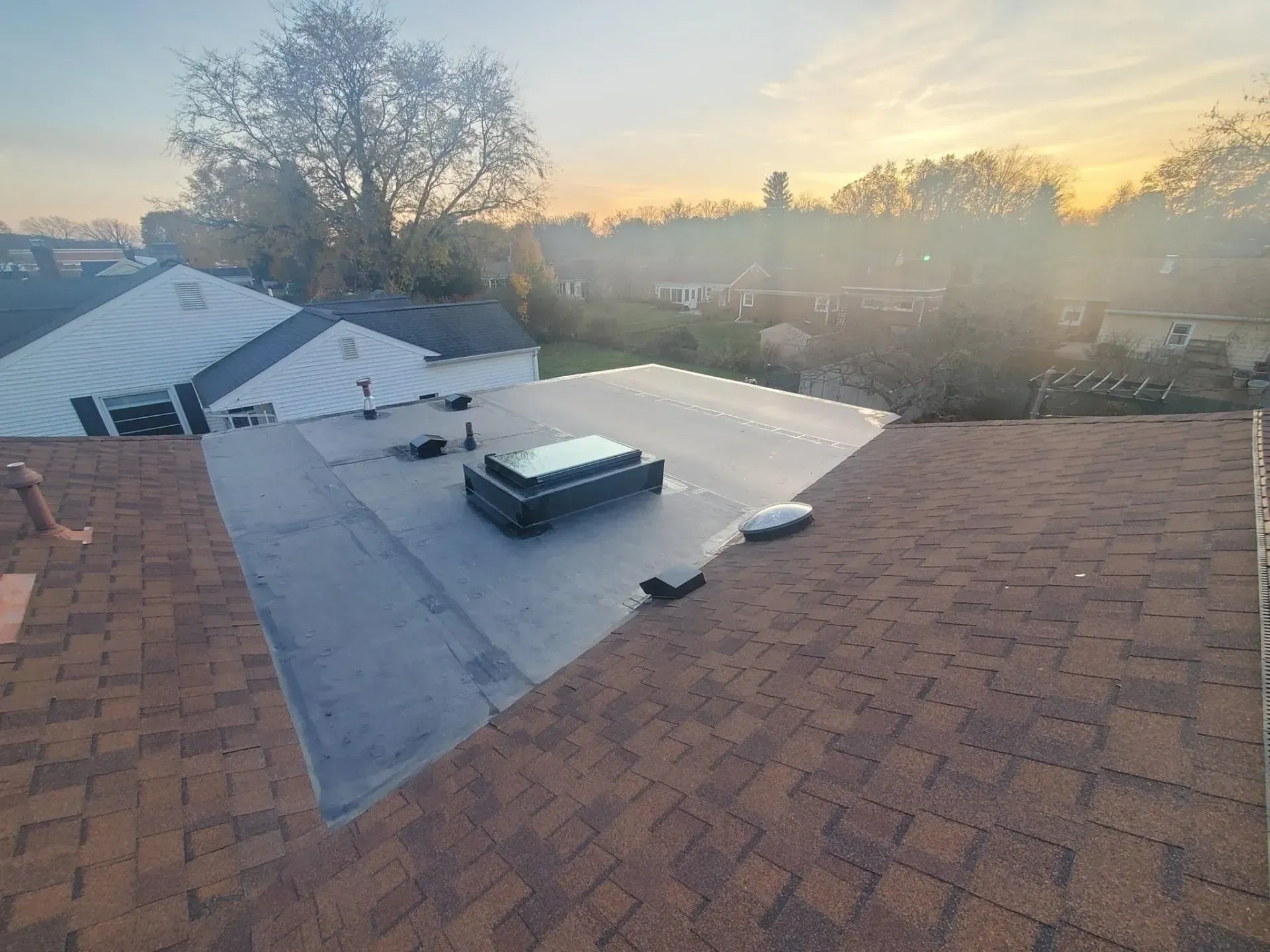 Brown shingle roof with black flat roof section and skylight.