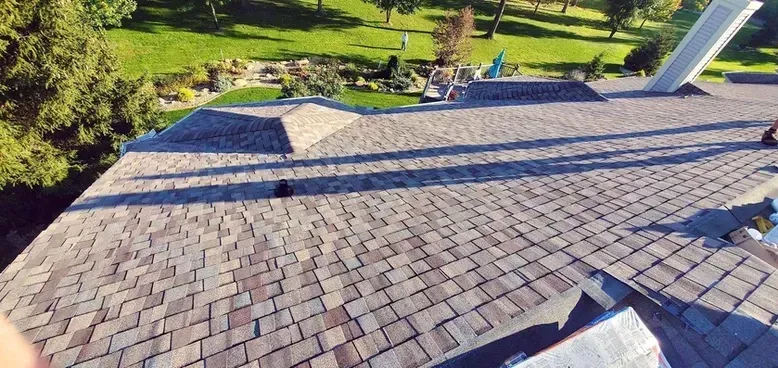 Overhead view of a roof with brown and gray shingles, sunlight casting long shadows.
