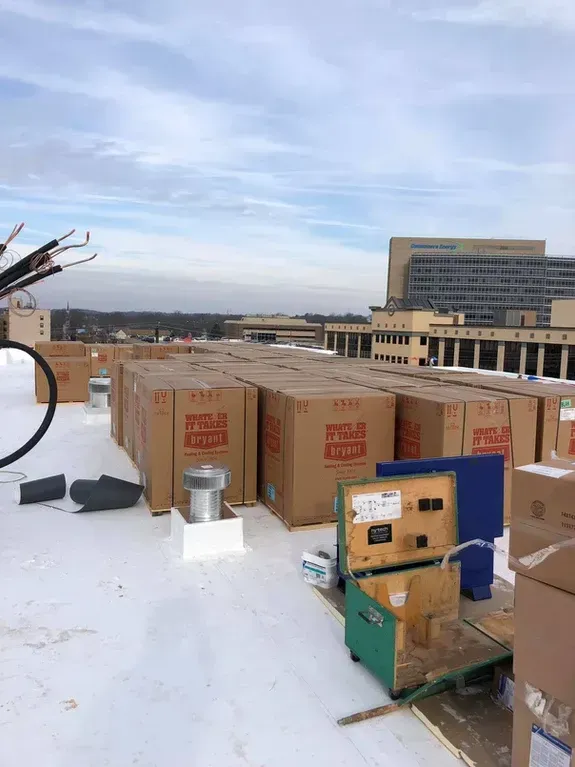 Cardboard boxes stacked on a white rooftop, possibly for HVAC installation. 