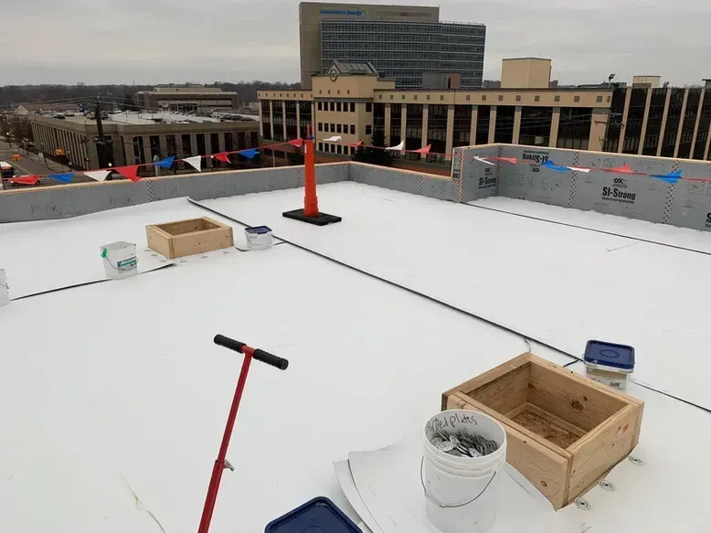 Rooftop with white surface, equipment, and buildings in the background.