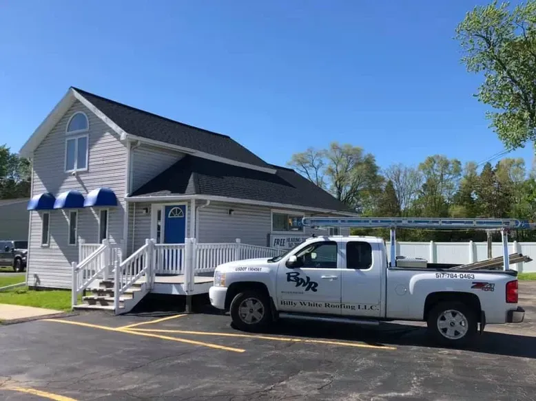White pickup truck parked in front of a gray office building with a blue awning and roof.